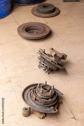 Old, used, rusty rear hubs, on which the brake pads of the parking brake are visible, and brake discs on the beige tiled floor of the car repair shop