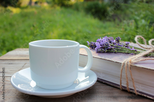 Cup of coffee and old book decorated with lavender flowers and tied with jute twine on wooden table. Copy space. Selective focus. Enjoying summer life
