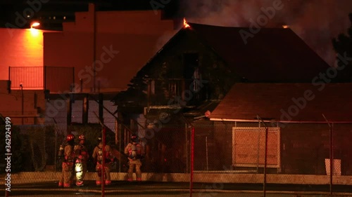 Firefighters and burning building with heavy smoke and flame on roof nighttime fire.