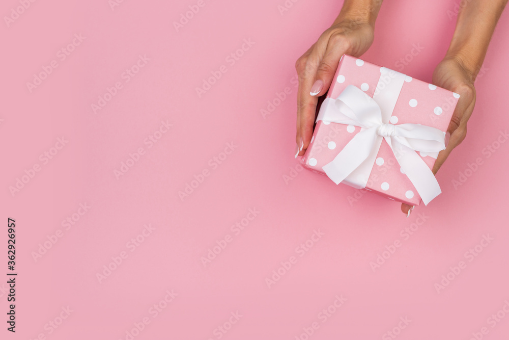 Hands holding craft paper gift box with a gift for Christmas, New Year, Valentine's Day or anniversary on a pink background, top view Hands holding craft paper gift box with a gift for Christmas, New Year, Valentine's Day or anniversary on a pink background, top view