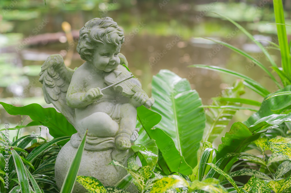Figurine of a little angel cupid playing the violin in the garden. Figurine of a little angel cupid playing the violin in the garden.