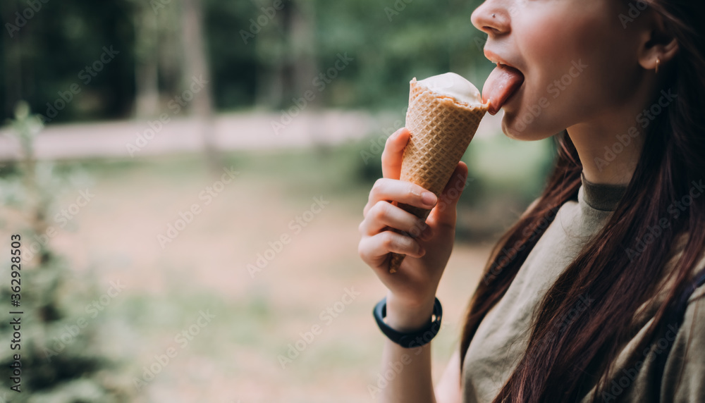 Young pretty woman holding ice cream in a waffle cone while walking along the street in the park alone. Young pretty woman holding ice cream in a waffle cone while walking along the street in the park alone.