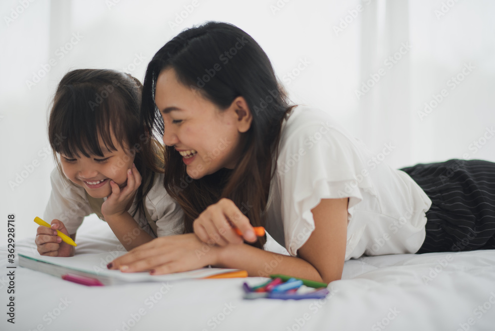 Love of young Asian mother and daughter lie on white bed and enjoy to play creative education drawing in bed room at home which smiling and felling happy. Asian love family live at home concept. Love of young Asian mother and daughter lie on white bed and enjoy to play creative education drawing in bed room at home which smiling and felling happy. Asian love family live at home concept.