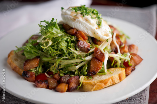 Salad. Frisee lettuce dress with olive oil and balsamic vinegar and topped with bacon lardons a fried egg and garnished with italian parsely and a toasted baguette. Served in a French Bistro.