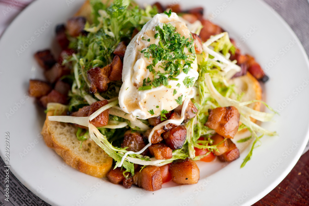 Salad. Frisee lettuce dress with olive oil and balsamic vinegar and topped with bacon lardons a fried egg and garnished with italian parsely and a toasted baguette. Served in a French Bistro. Salad. Frisee lettuce dress with olive oil and balsamic vinegar and topped with bacon lardons a fried egg and garnished with italian parsely and a toasted baguette. Served in a French Bistro.