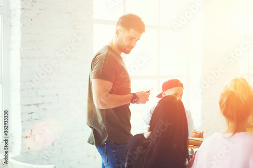 Bearded handsome male member of skilled team talking with female colleagues and discussing general work concepts in sunshine studio.Good looking man sharing experience and giving advices for partner