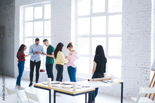 Group of male and female students spending leisure on break browsing and chatting in social network instead of talking with each other, coworkers using gadgets and wifi ignoring social conversation