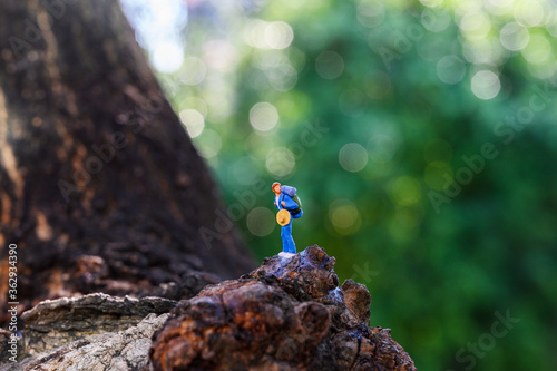 Miniature adventure travel concept : Small toy figure backpacker is Climbing at the mountain with background of the forest.