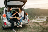 Young Stylish Traveling Hipsters Having Fun Sitting in Car Trunk and Eating Pizza, Travel and Road Trip Concept