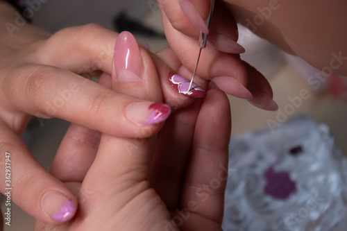 the process of doing manicure. Closeup of hands of professional manicurist, painting little flowers on nails. Concept of doing manicure. beauty concept. Gel polish, shellac