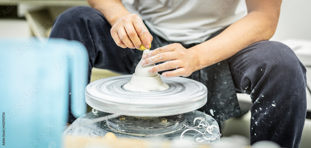 koreanischer Keramik Meister dreht an der Drehscheibe und befeuchtet die Keramikmasse mit dem Schwamm
