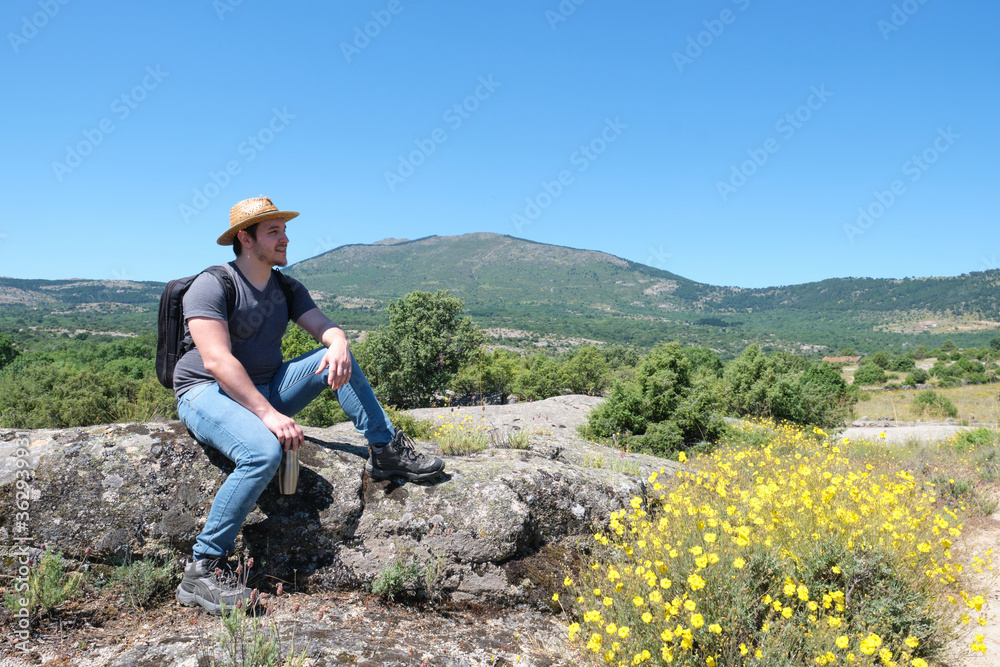 Young caucasian man with a straw hat sitting in a rock and enjoying the view. Mushroom rocks path (Ruta de las Piedras Seta), Madrid, Spain.