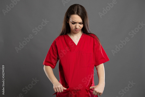 Sad nurse looks at her empty pockets wearing red scrubs © Catalin Pop