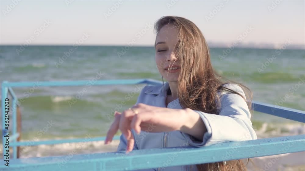 Young disabled woman in wheelchair shows fingers step walking by the handrails on the ramp for people with disabilities near the sea