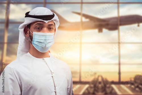 Slika na platnu Arabic traveler business man wearing mask waiting to board into airplane, standing in departure terminal in airport
