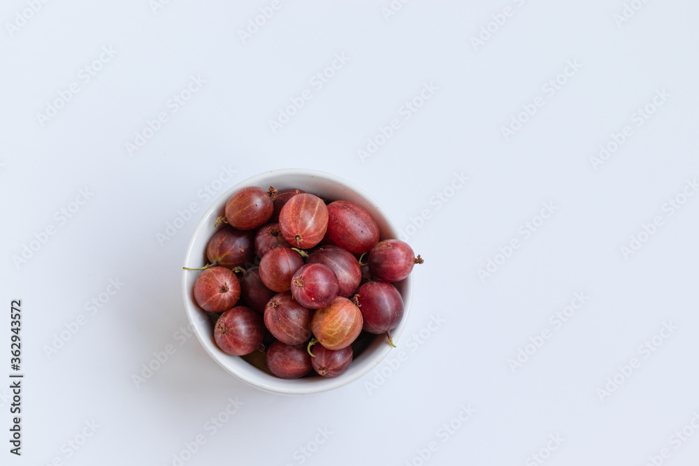 Fresh gooseberries in a ceramic bowl on a white table. View from above. Fresh gooseberries in a ceramic bowl on a white table. View from above.