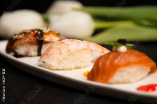 Set of Japanese Ebi Nigiri Sushi with tiger shrimp in focus near nigiri Sake with salmon and Unagi with eel. white plate with colourful food decoration painting spots. Asian restaurant seafood menu 