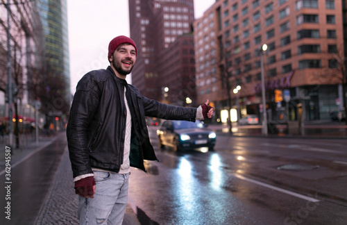 Young handsome happy hipster young man traveler hitchhiking along on road in the city.