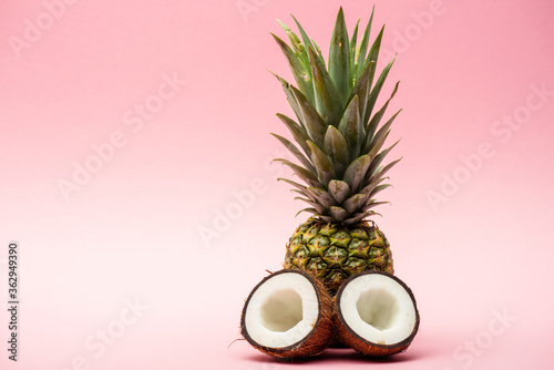 ripe pineapple and fresh coconut halves on pink background