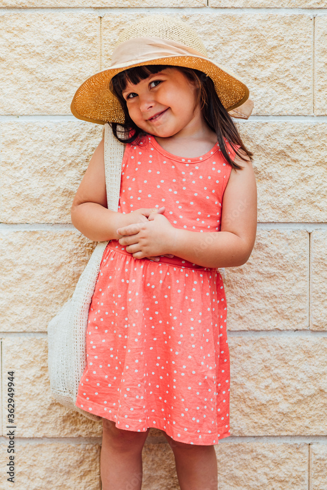Portrait of a little black-haired girl smiling with summer dress, hat and bag