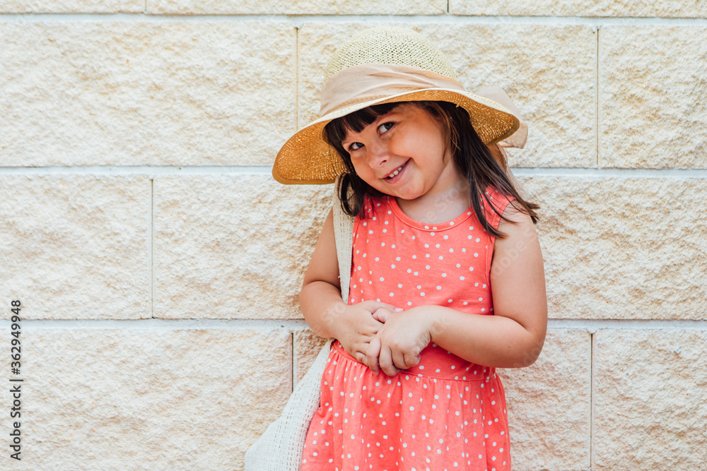 Portrait of a little black-haired girl smiling with summer dress, hat and bag