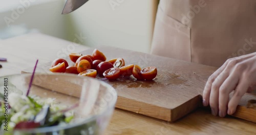 Woman cutting and adding cherry tomatoes into salad