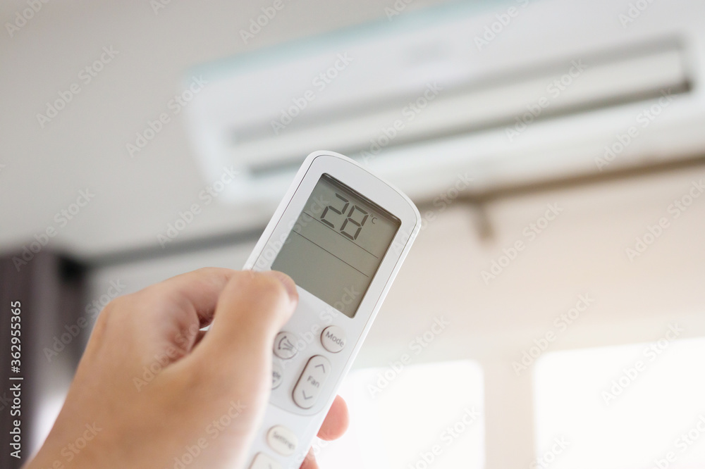 Hand with remote control directed on air conditioner inside the room Hand with remote control directed on air conditioner inside the room