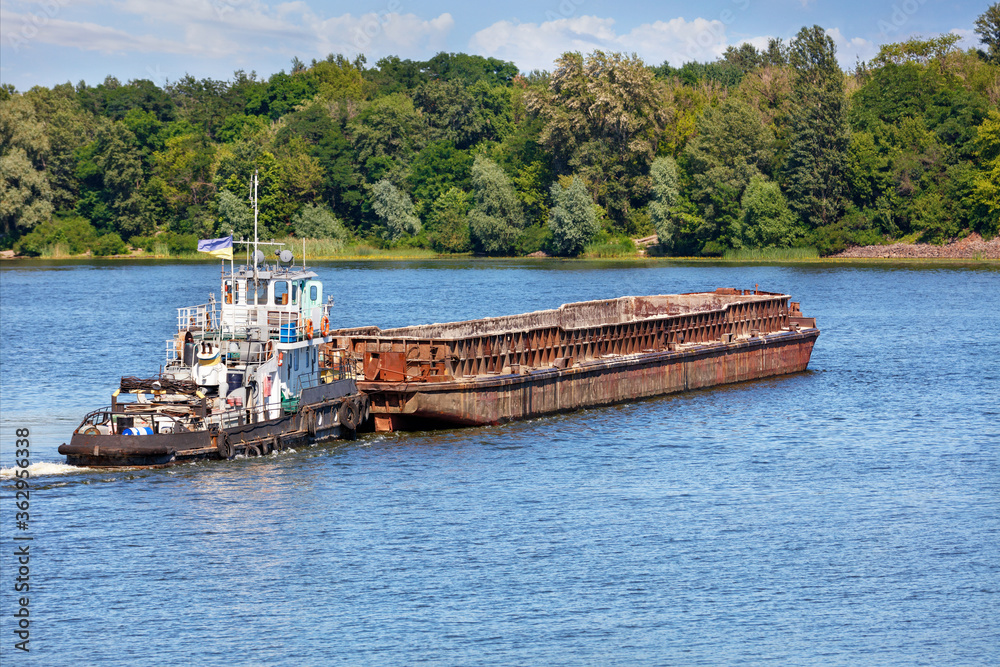 A river tugboat with an empty rusty barge goes crosses a wide river. A river tugboat with an empty rusty barge goes crosses a wide river.