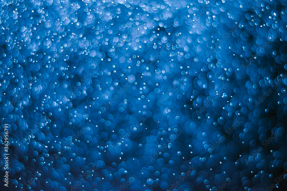 Bokeh of water drops reflects light like bubble in deep sea on a black background. Abstract defocused dark blue background.