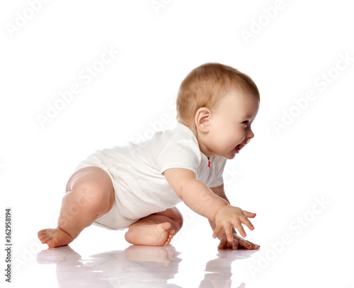 Adorable positive little baby infant in white cotton body and barefoot trying to creep on floor, smiling and looking aside