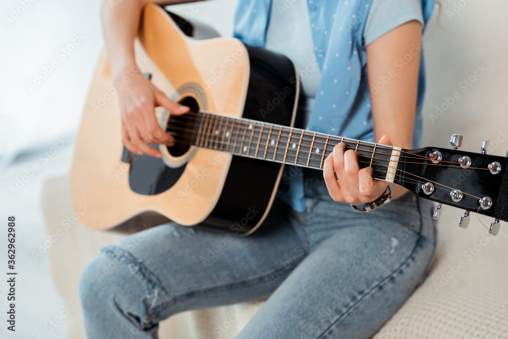 Cropped view of young woman performing on acoustic guitar on sofa