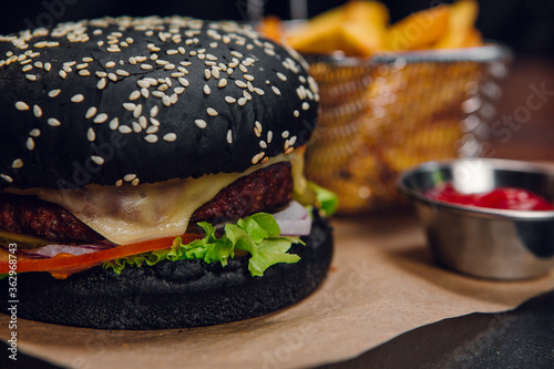 Black burger with fries and ketchup on a table in a restaurant. Fast food  junk food