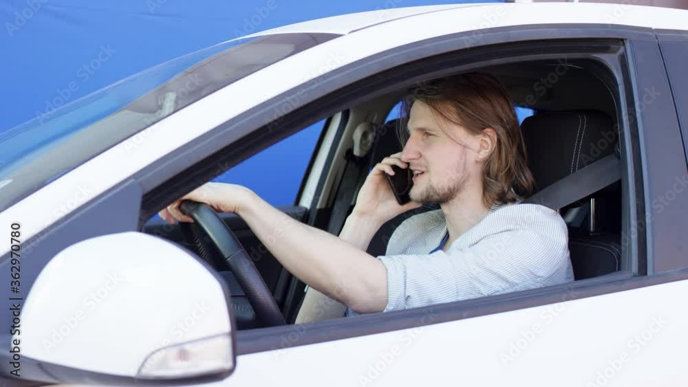 Young man is discussing amazing news on his cellphone. Guy in casual clothes is driving a white car against blue screen background. Young man is discussing amazing news on his cellphone. Guy in casual clothes is driving a white car against blue screen background.