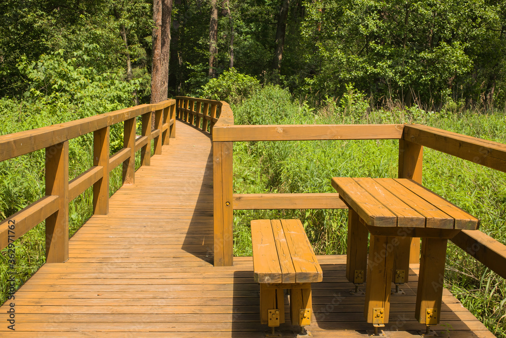 A place of rest with a wooden bench and a table in the middle of wild nature on a sunny summer day. A place of rest with a wooden bench and a table in the middle of wild nature on a sunny summer day.