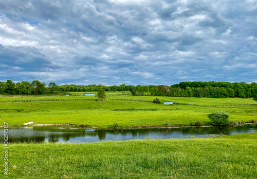 Countryside Landscape with Green Fields, Cloudy Sky and Stream