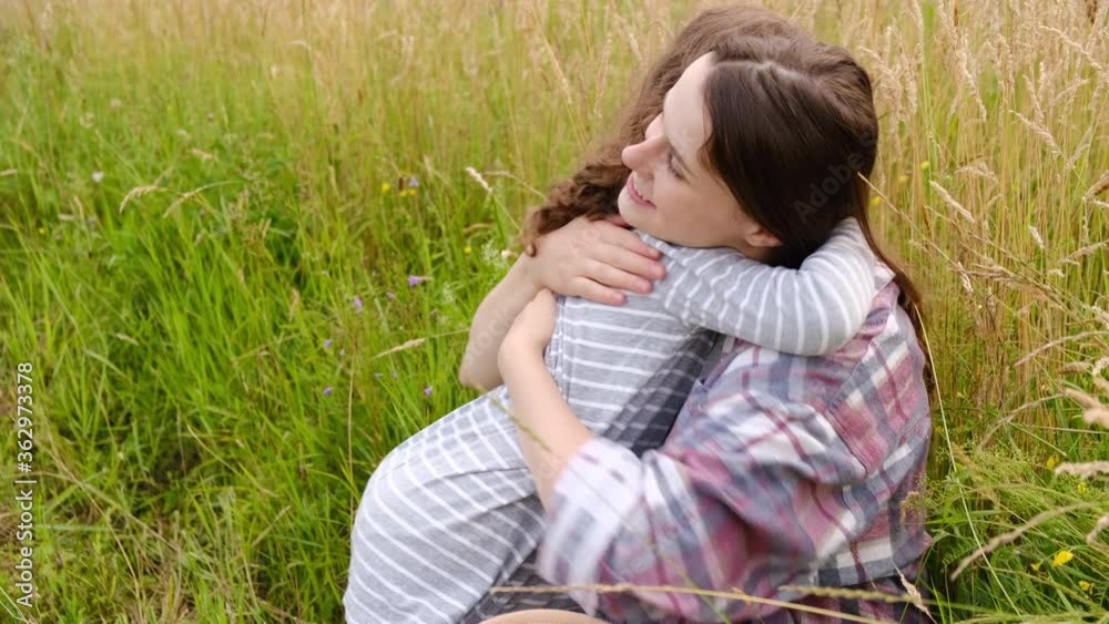 Happy cute affectionate little kid girl hugging young mother sitting on grass in summer park, adorable small child daughter embrace mum cuddling enjoy tender sweet moment. Concept friendship day Happy cute affectionate little kid girl hugging young mother sitting on grass in summer park, adorable small child daughter embrace mum cuddling enjoy tender sweet moment. Concept friendship day