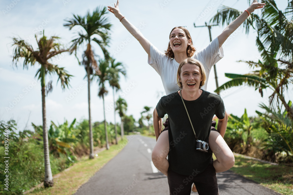 A man carrying his girlfriend in the middle of the road surrounded by tropical exotic view