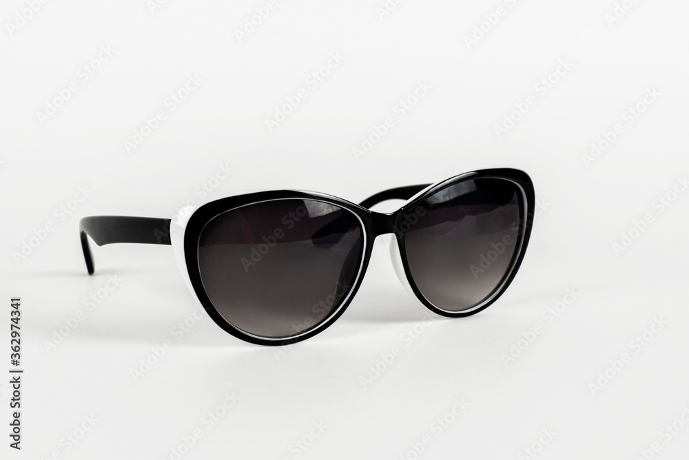 Beautiful women's sunglasses on a light background with a light shadow, glasses in black and white, these glasses are relevant in the sunshine