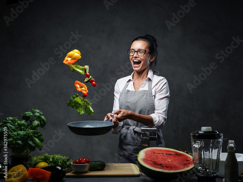 Fotografie Emotional mature female chef tossing chopped vegetables from a pan