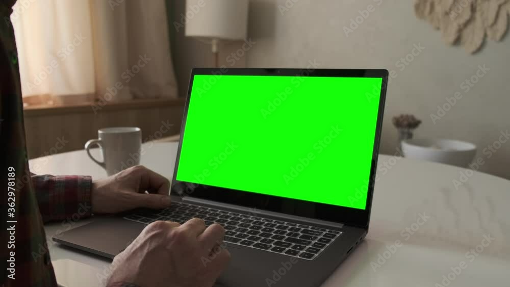 Male using notebook with chroma key at home. Man working on laptop with green screen. Stay home. Over shoulder view. 4K, UHD Male using notebook with chroma key at home. Man working on laptop with green screen. Stay home. Over shoulder view. 4K, UHD