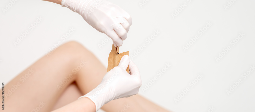 Human hands in protective gloves holding craft envelope with medical or beauty tools on background of female legs Human hands in protective gloves holding craft envelope with medical or beauty tools on background of female legs