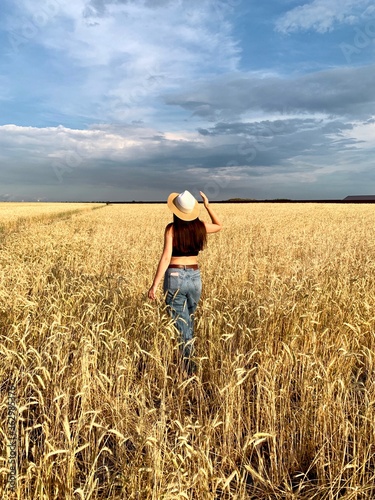 Young happy beautiful slender girl with long hair and a hat in a wheat field. Summer landscape