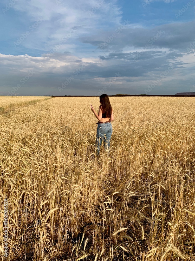 Young happy beautiful slender girl with long hair and a hat in a wheat field. Summer landscape