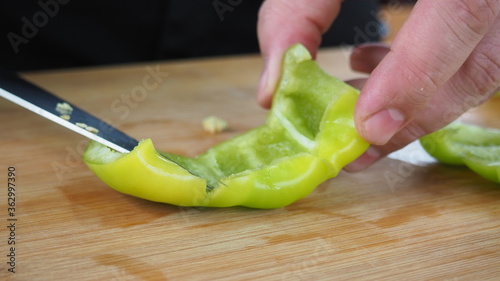 the cook slices red and green peppers on a wooden Board