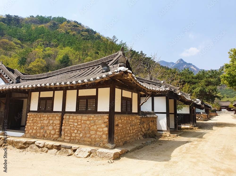 Small Korean buildings near forested mountains under a blue sky at daytime Small Korean buildings near forested mountains under a blue sky at daytime