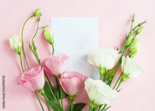 Fototapeta Naklejka Na Ścianę i Meble -  A sheet of paper lies horizontally on pink paper, flowers of eustoma (lisianthus) Top view, Copy space. Concept Mother's Day, Family Day, Valentine's Day