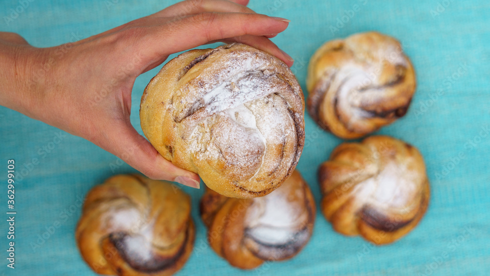 Top view of womens hand holding a sweet bun over the blurred background with other buns. Bakery concept. Space for text. Top view of womens hand holding a sweet bun over the blurred background with other buns. Bakery concept. Space for text.