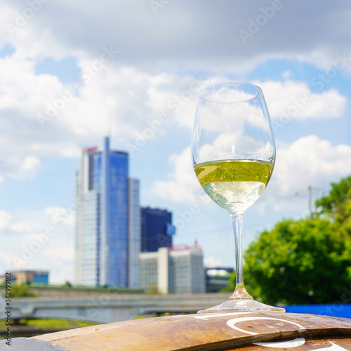 Glass of white wine with reflection on the blurred cityscape and dramatic sky background. Space for text. Wine concept.