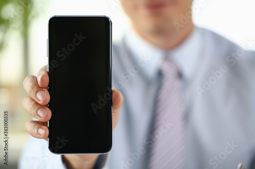 Close up of businessman holding smartphone while demonstrating it at the camera. Copy space on screen