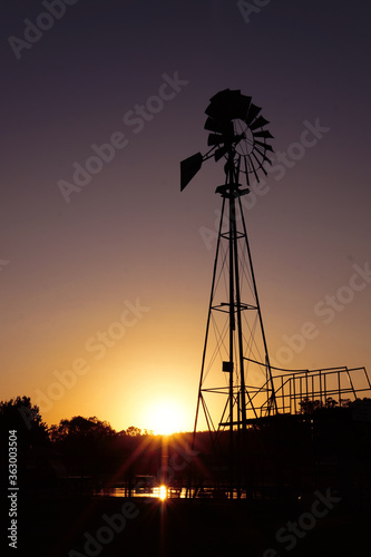 Sunset landscape in countryside. A windmill silhouette in a farm located in Brandsen, BUenos Aires, Argentina.  In the background a few small trees and the sun almost hidden. Taken on a warm summer af